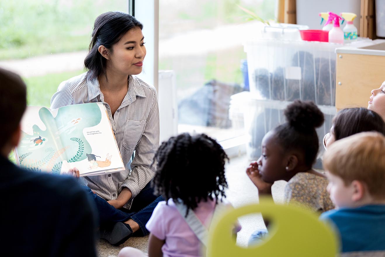 Confident female librarian reads young schoolchildren a picture book during story time.