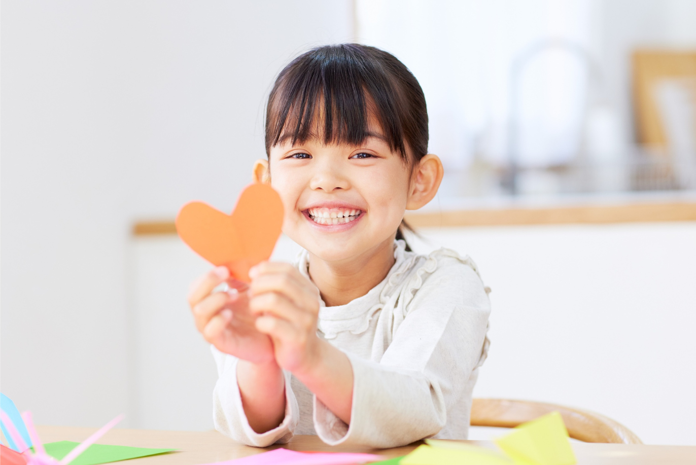 Young girl holding orange paper heart.